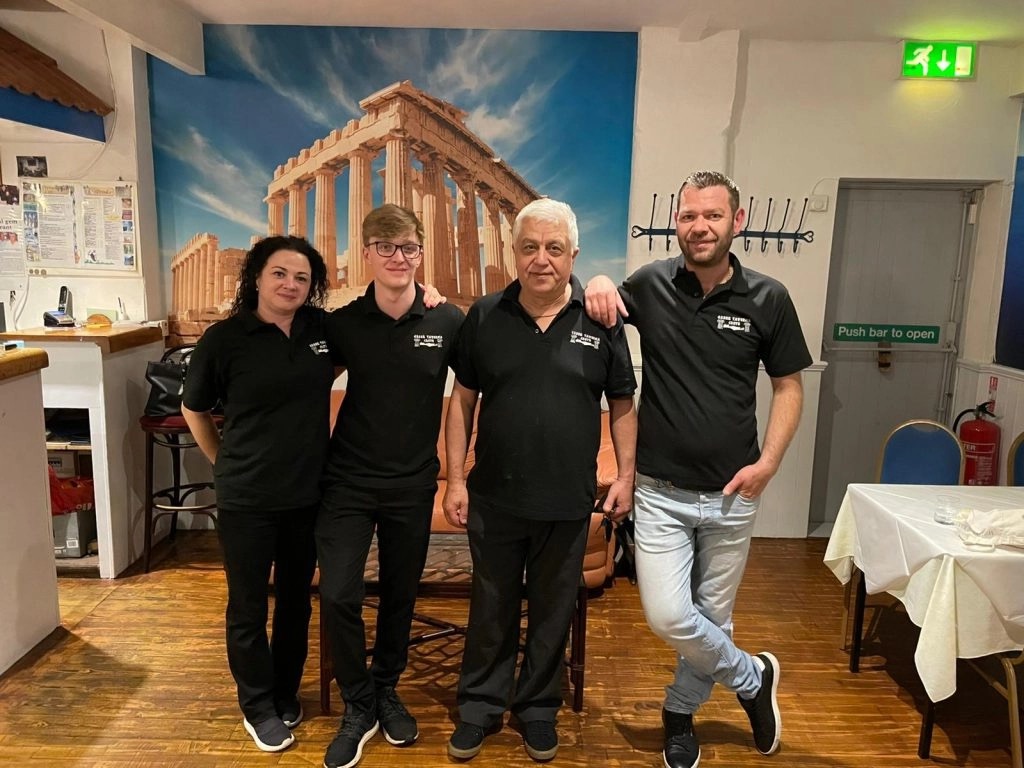 The Crete taverna team posing in front of the Parthenon mural
